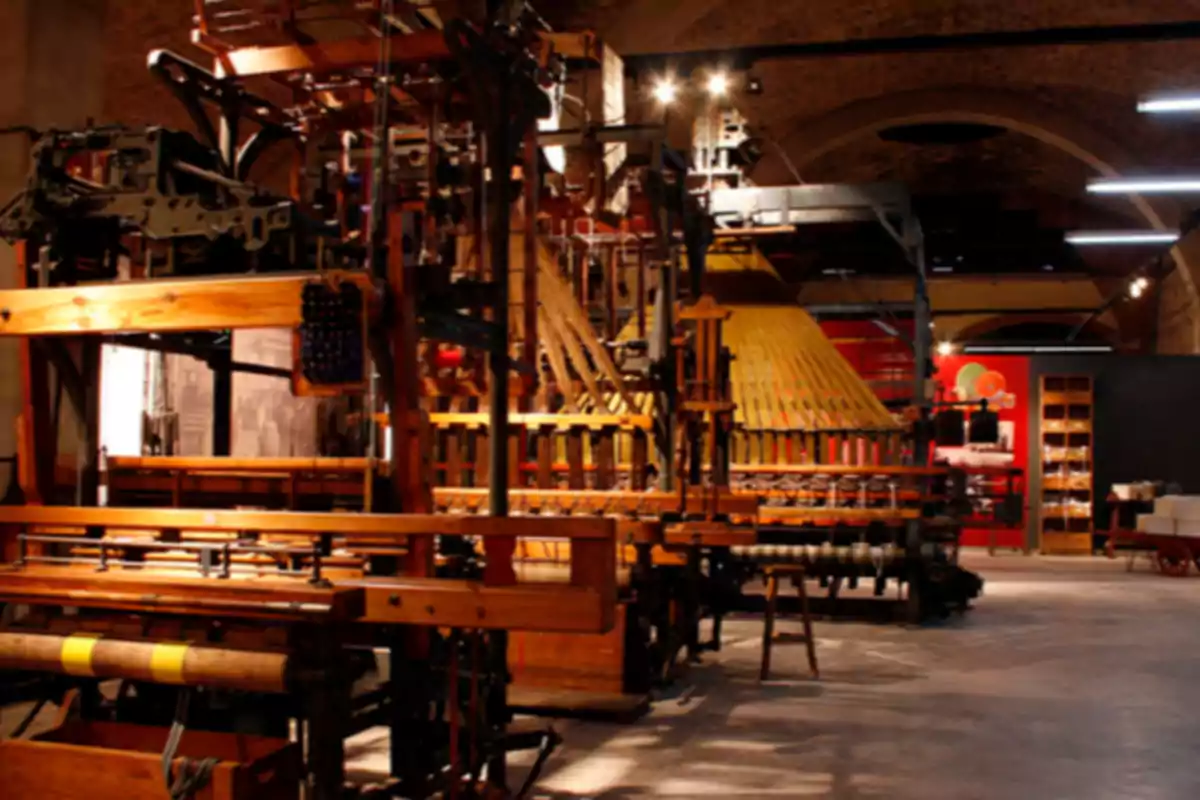 Antiga màquina tèxtil de fusta i metall exposada en un museu industrial il·luminat Antiga màquina tèxtil de fusta i metall exposada en un museu industrial il·luminat