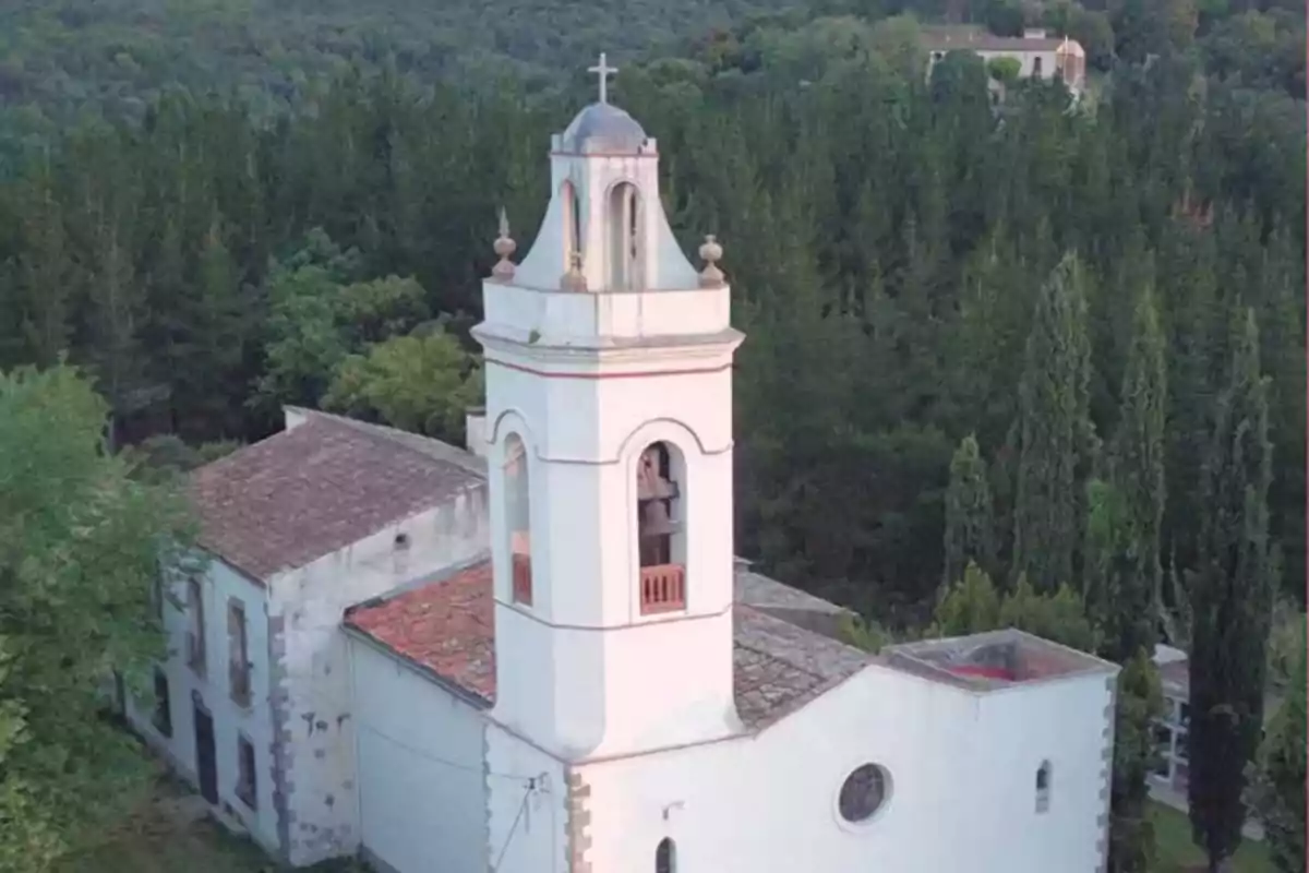 Iglesia antigua de paredes blancas con campanario rodeada de árboles y vegetación Iglesia antigua de paredes blancas con campanario rodeada de árboles y vegetación