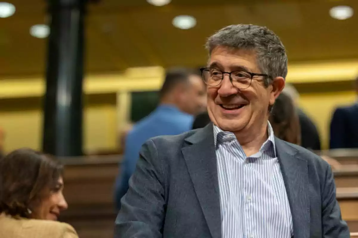Patxi López con cabello canoso y gafas sonriendo en un ambiente interior con otras personas al fondo Patxi López con cabello canoso y gafas sonriendo en un ambiente interior con otras personas al fondo