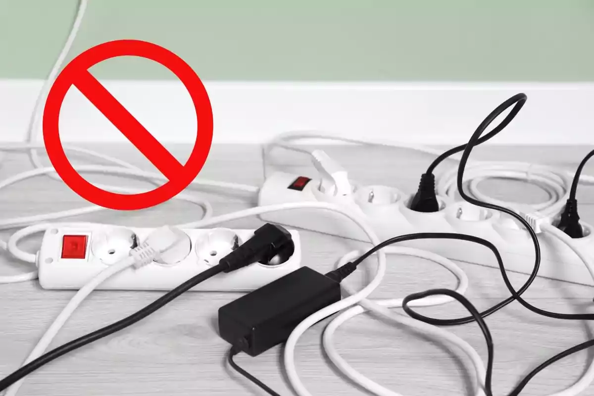 Diverses regletes elèctriques a terra amb molts cables connectats i un símbol de prohibit de color vermell indicant perill o advertència Diverses regletes elèctriques a terra amb molts cables connectats i un símbol de prohibit de color vermell indicant perill o advertència