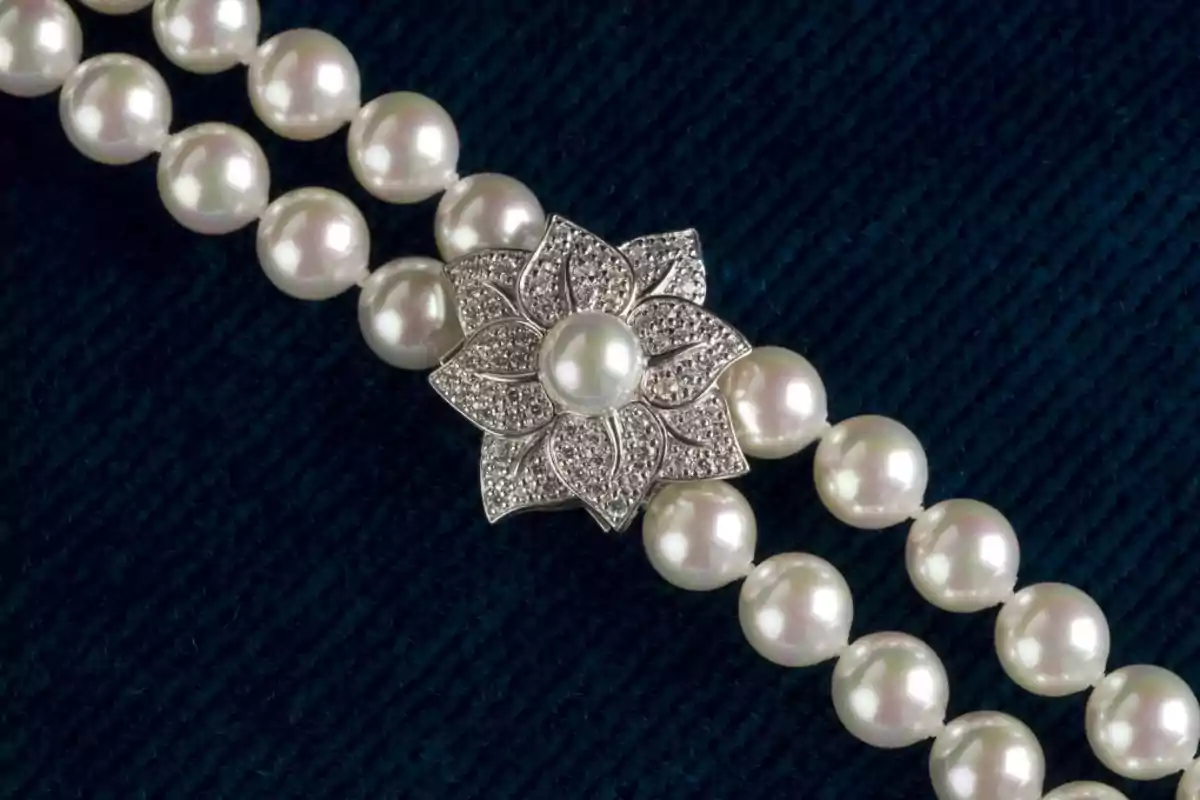Collar de perlas blancas con broche en forma de flor sobre fondo azul oscuro Collar de perlas blancas con broche en forma de flor sobre fondo azul oscuro