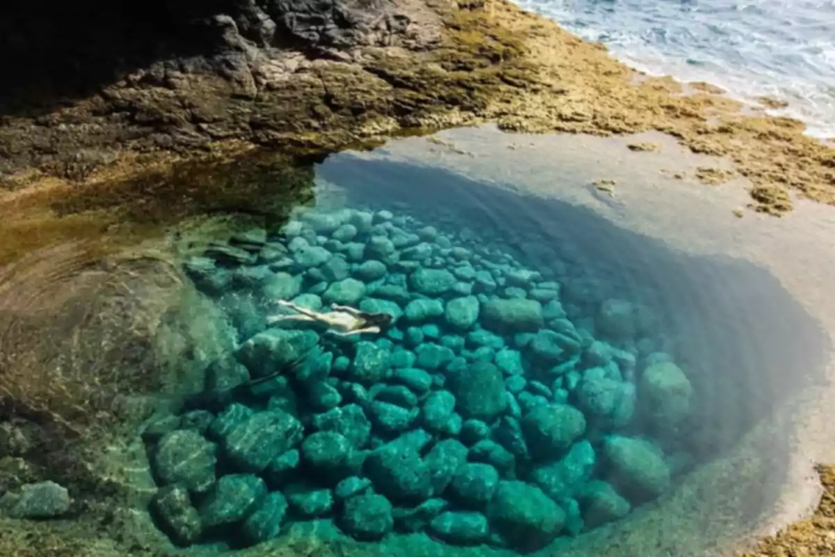 Persona nadando en una piscina natural de agua cristalina rodeada de rocas y el mar al fondo Persona nadando en una piscina natural de agua cristalina rodeada de rocas y el mar al fondo