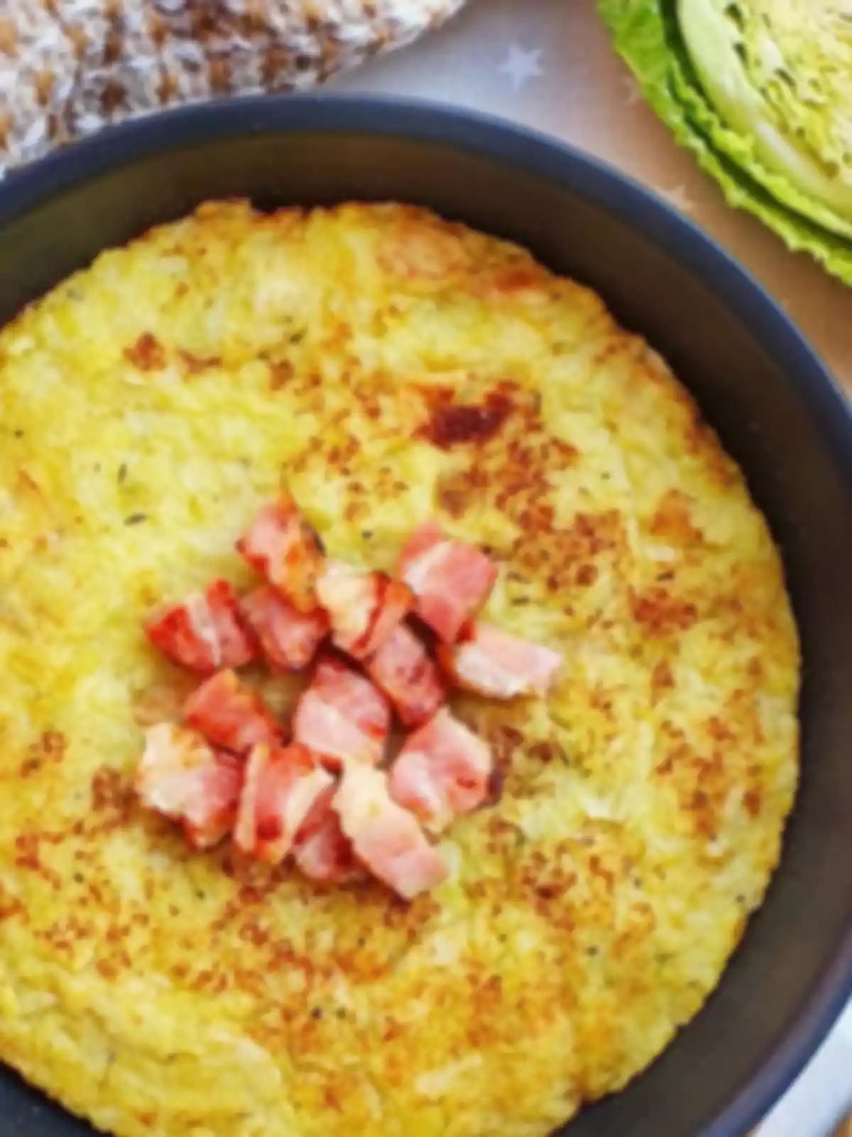Tortilla dorada de papas servida en sartén con trozos de tocino en el centro, acompañada de pan y lechuga al fondo Tortilla dorada de papas servida en sartén con trozos de tocino en el centro, acompañada de pan y lechuga al fondo