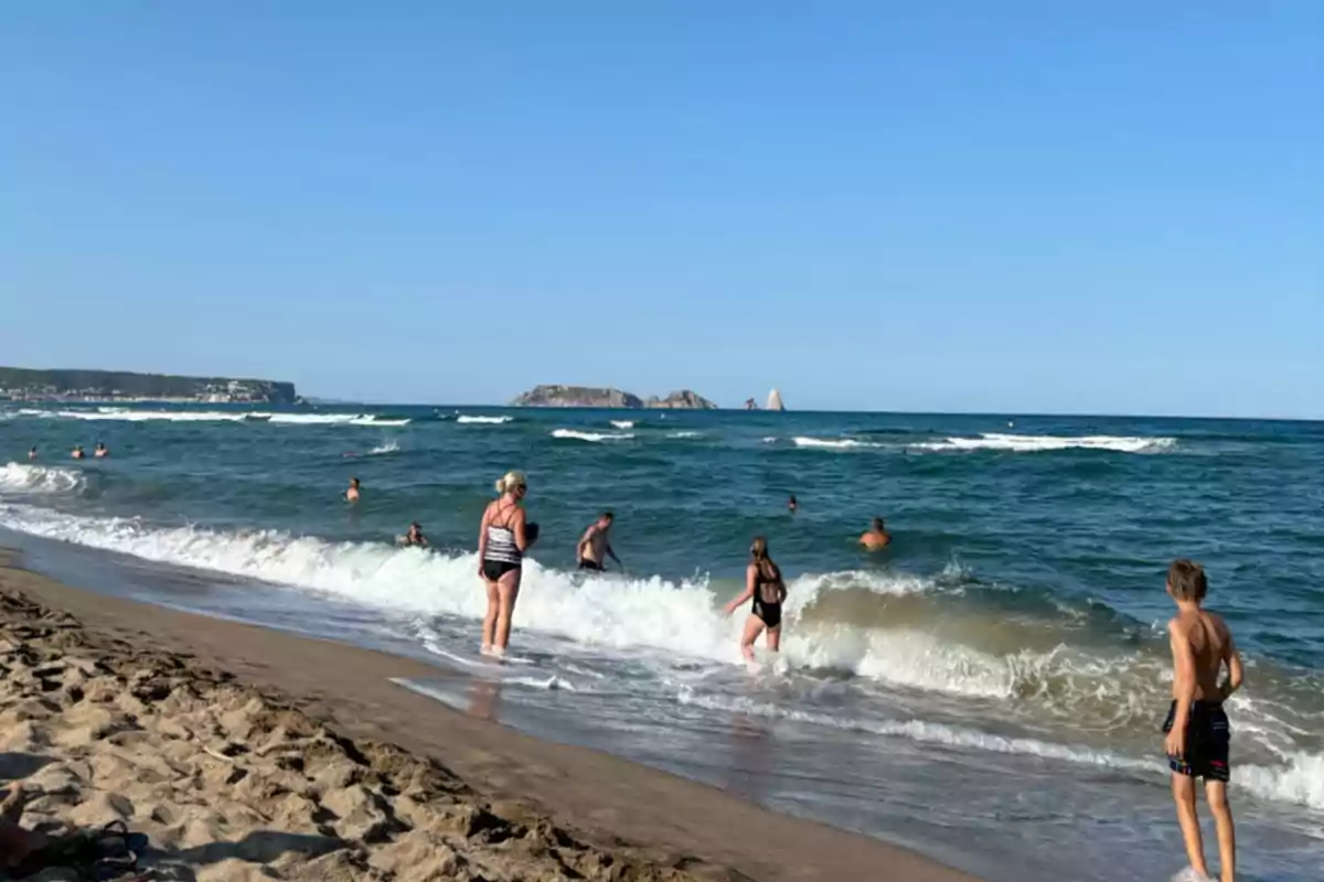 Personas disfrutando en la orilla de una playa con olas y un cielo despejado Personas disfrutando en la orilla de una playa con olas y un cielo despejado