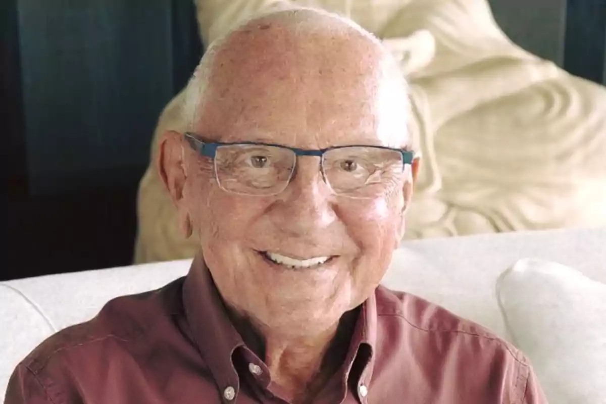 Older man with glasses and a brown jersey smiling while sitting on a light-colored sofa Older man with glasses and a brown jersey smiling while sitting on a light-colored sofa