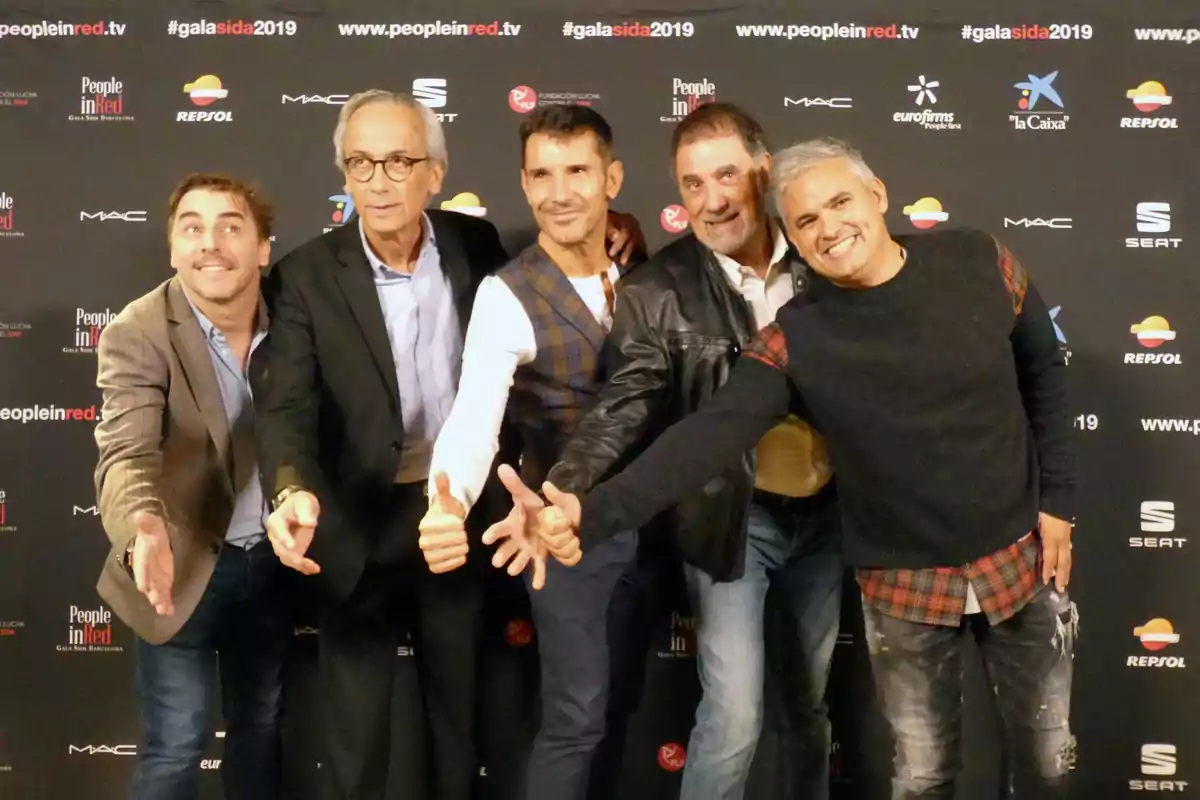 Cinc homes posen somrients davant d’un fons de patrocinadors en un esdeveniment, estenent les mans cap a la càmera. Cinc homes posen somrients davant d’un fons de patrocinadors en un esdeveniment, estenent les mans cap a la càmera.