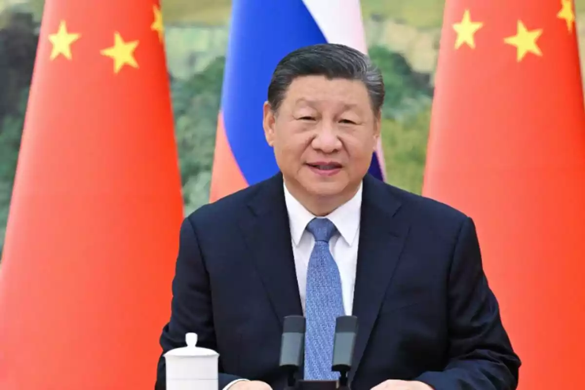 Home amb vestit fosc i corbata blava parlant davant de micròfons amb banderes de la Xina i Rússia de fons Home amb vestit fosc i corbata blava parlant davant de micròfons amb banderes de la Xina i Rússia de fons