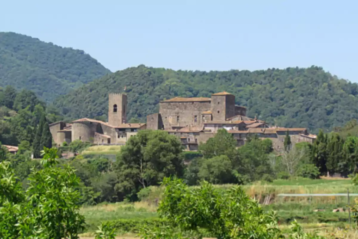 Vista d’un poble medieval envoltat de vegetació i muntanyes en un dia assolellat
