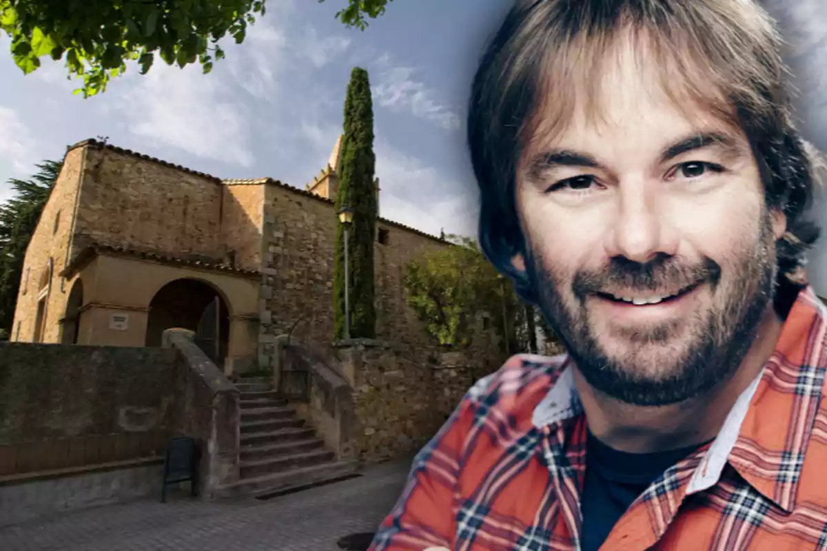Home somrient amb camisa de quadres en primer pla i una església de pedra al fons
