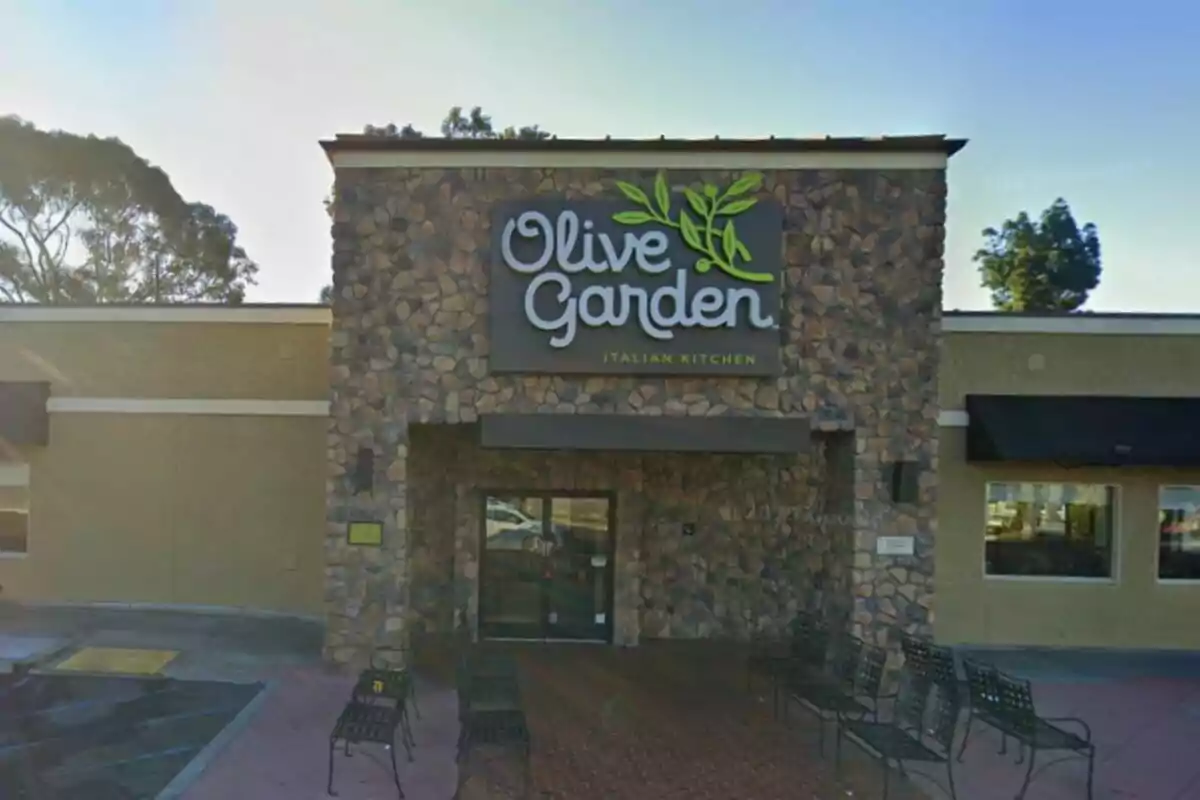 Fachada de un restaurante Olive Garden con paredes de piedra y bancos metálicos en la entrada Fachada de un restaurante Olive Garden con paredes de piedra y bancos metálicos en la entrada
