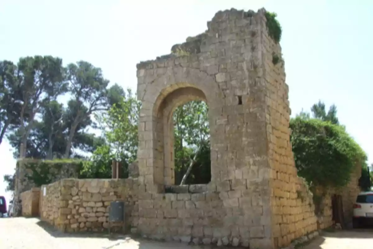 Ruïna d’una antiga construcció de pedra amb un gran arc al centre envoltada de vegetació i arbres Ruïna d’una antiga construcció de pedra amb un gran arc al centre envoltada de vegetació i arbres