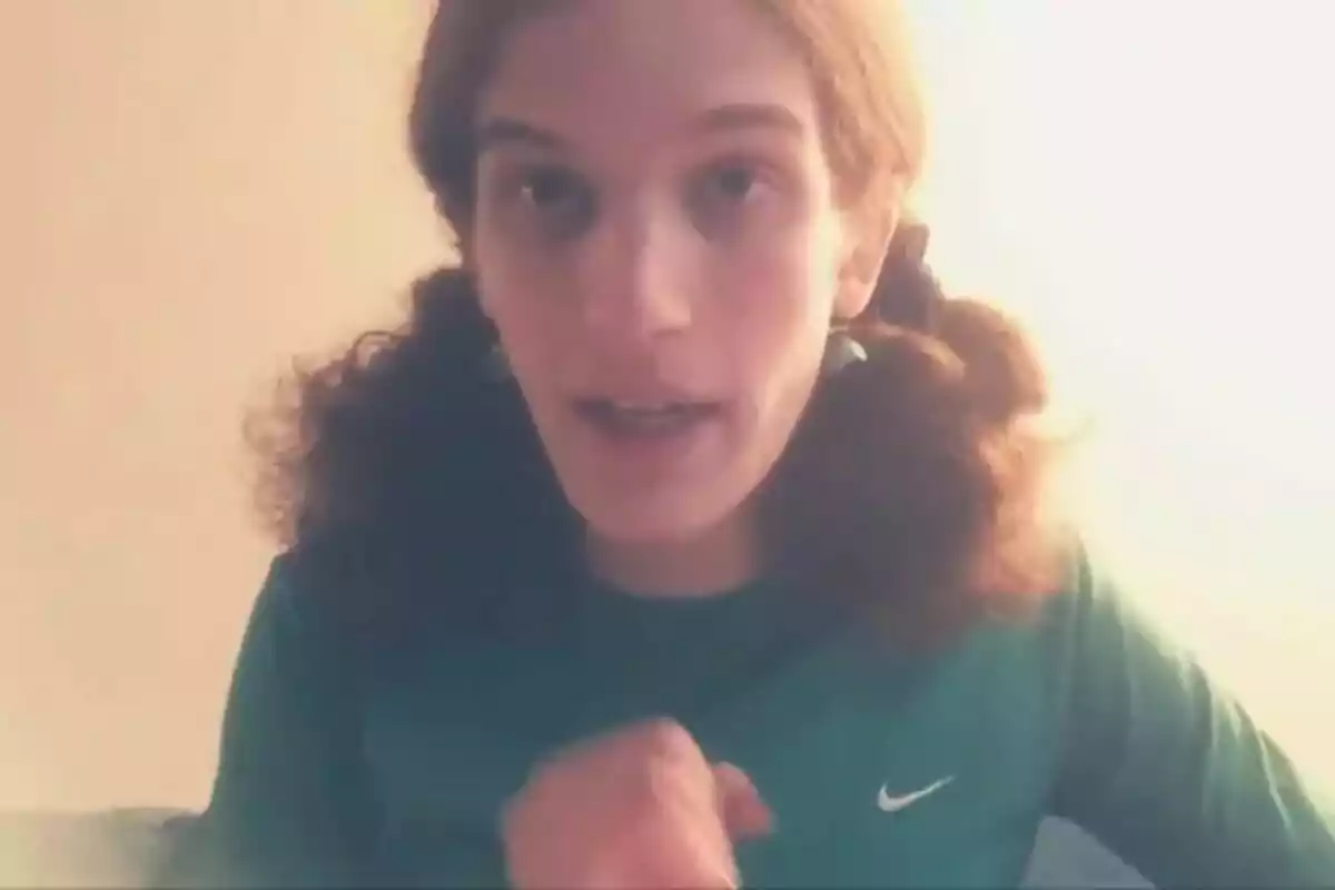 Persona con cabello largo y rizado recogido en dos coletas, usando una camiseta verde con el logo de Nike, mirando hacia la cámara en un ambiente iluminado.