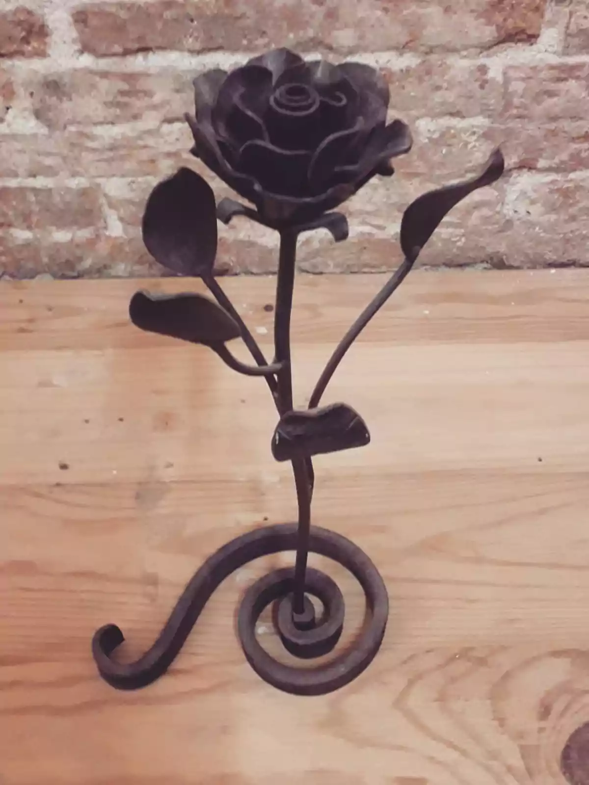 Escultura de una rosa hecha de metal sobre una mesa de madera con fondo de ladrillos Escultura de una rosa hecha de metal sobre una mesa de madera con fondo de ladrillos