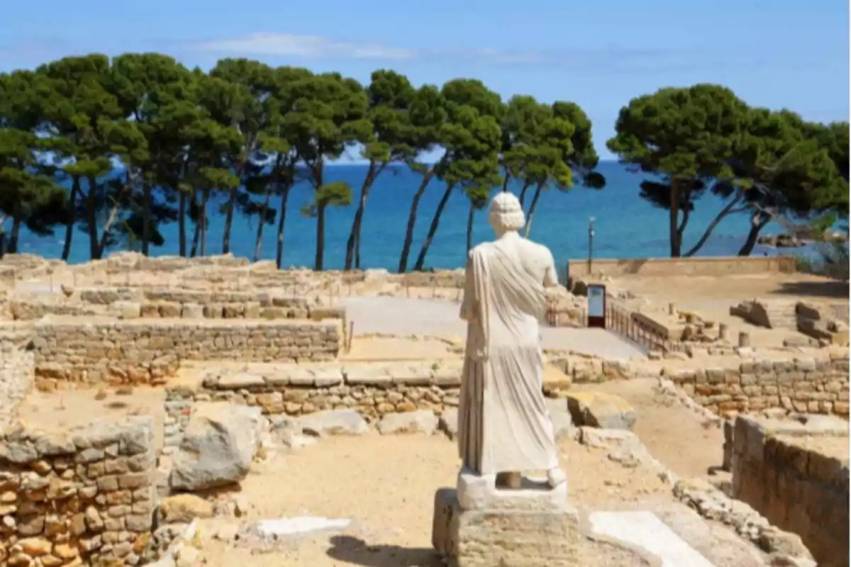 Ruïnes antigues vora el mar amb una estàtua d’esquena i arbres al fons Ruïnes antigues vora el mar amb una estàtua d’esquena i arbres al fons