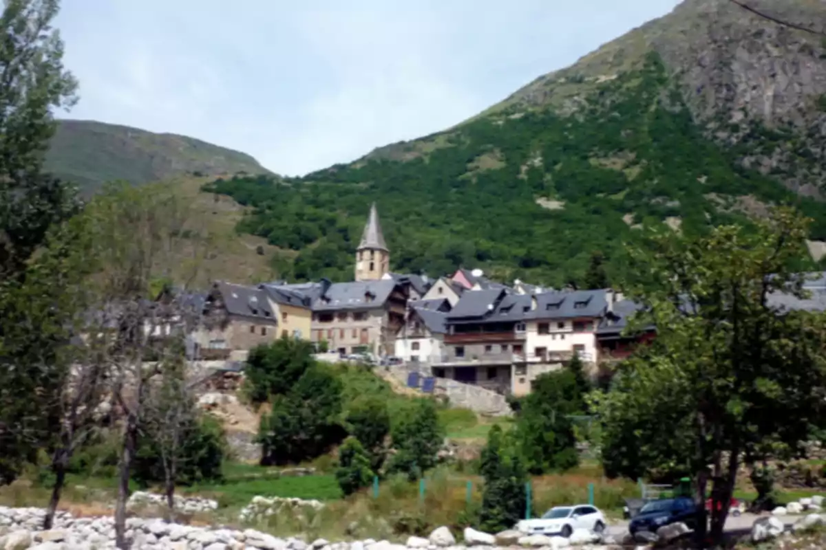 Pueblo de montaña rodeado de vegetación con casas de tejados oscuros y una iglesia con torre en el centro Pueblo de montaña rodeado de vegetación con casas de tejados oscuros y una iglesia con torre en el centro