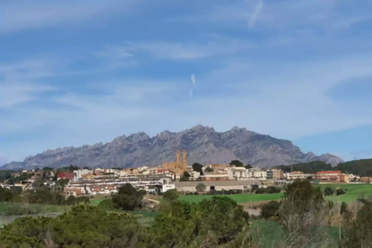 Pueblo rodeado de vegetación con una iglesia destacada y montañas rocosas al fondo bajo un cielo azul Pueblo rodeado de vegetación con una iglesia destacada y montañas rocosas al fondo bajo un cielo azul