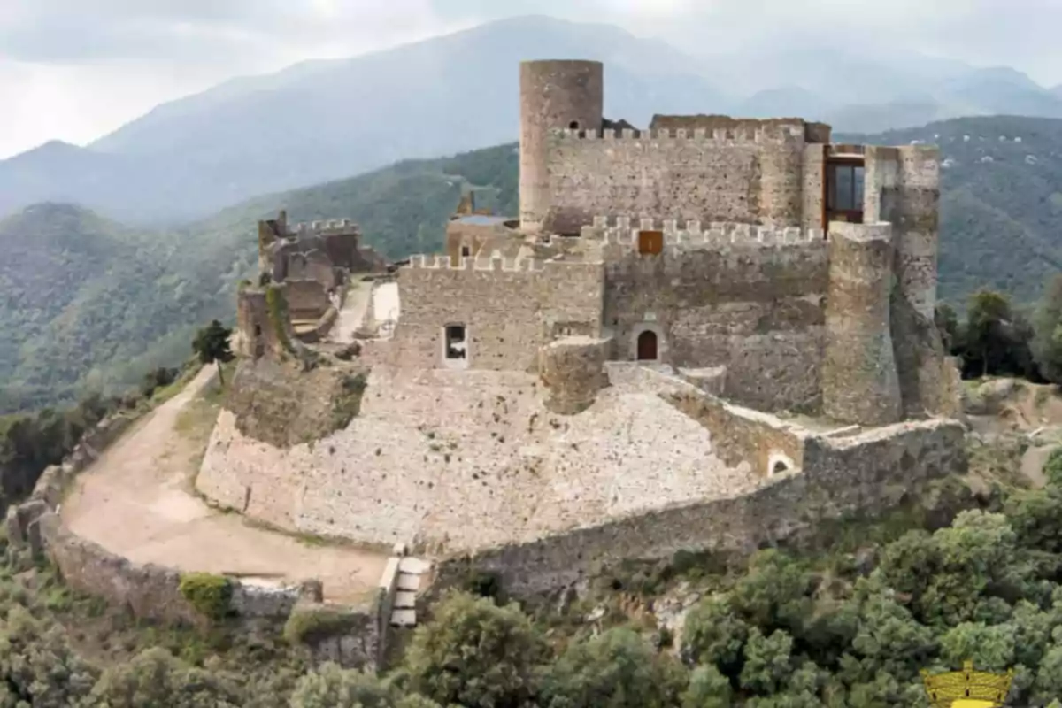 Castillo de piedra en la cima de una colina rodeado de montañas y vegetación Castillo de piedra en la cima de una colina rodeado de montañas y vegetación