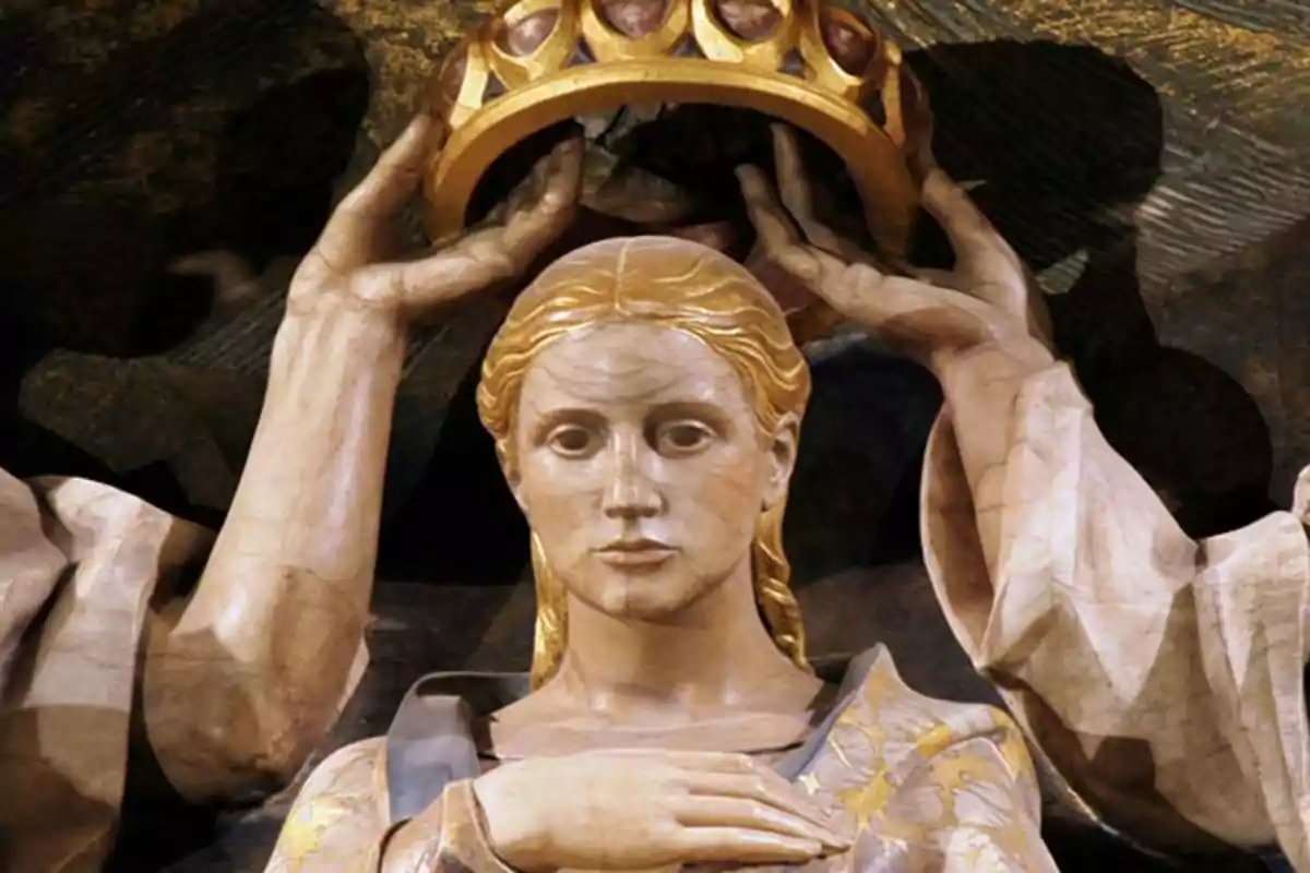 Escultura d’una figura femenina amb expressió serena a qui col·loquen una corona daurada sobre el cap Escultura d’una figura femenina amb expressió serena a qui col·loquen una corona daurada sobre el cap