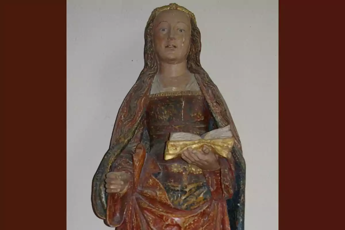 Escultura d’una dona amb túnica colorida i mantell, sostenint un llibre obert en una mà Escultura d’una dona amb túnica colorida i mantell, sostenint un llibre obert en una mà