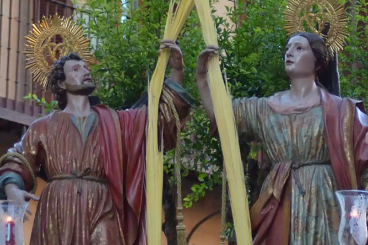 Dues figures religioses vestides amb túniques i aurèoles daurades sostenen palmes llargues davant d’un fons de vegetació i edificis. Dues figures religioses vestides amb túniques i aurèoles daurades sostenen palmes llargues davant d’un fons de vegetació i edificis.