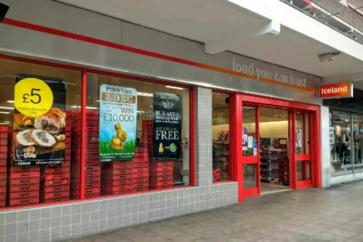 Facade of an Iceland store with red doors and frames, promotional signs in the windows, and the slogan Facade of an Iceland store with red doors and frames, promotional signs in the windows, and the slogan