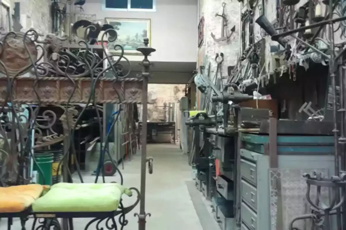Taller de herrería antiguo con herramientas y muebles de metal, bancos con cojines y paredes decoradas con objetos de hierro Taller de herrería antiguo con herramientas y muebles de metal, bancos con cojines y paredes decoradas con objetos de hierro