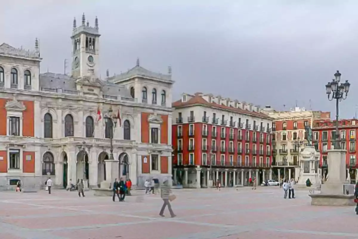Plaza amplia con edificios históricos de fachada roja y blanca, personas caminando y una farola antigua en el centro Plaza amplia con edificios históricos de fachada roja y blanca, personas caminando y una farola antigua en el centro