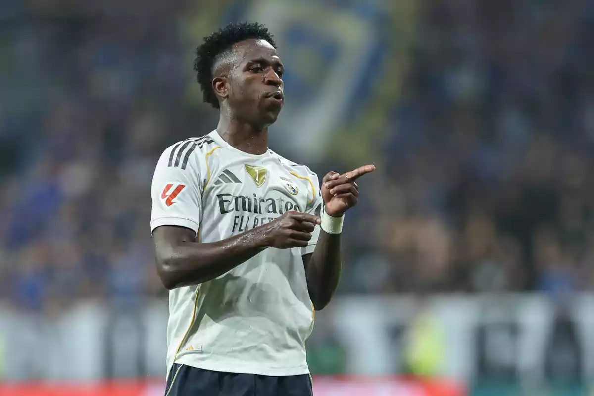Vinicius celebrating during a match, pointing with both hands and with the stadium blurred in the background. Vinicius celebrating during a match, pointing with both hands and with the stadium blurred in the background.
