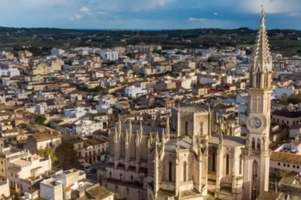 Vista aérea de una ciudad con una iglesia de estilo gótico y un campanario destacado entre edificios bajos y paisaje al fondo Vista aérea de una ciudad con una iglesia de estilo gótico y un campanario destacado entre edificios bajos y paisaje al fondo