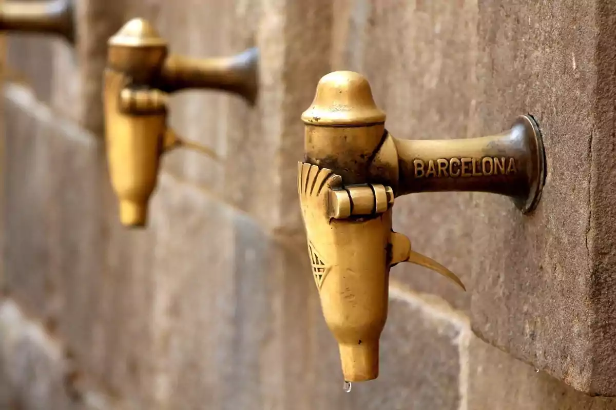Grifo antiguo de bronce en una pared de piedra con la palabra Barcelona grabada y una gota de agua cayendo