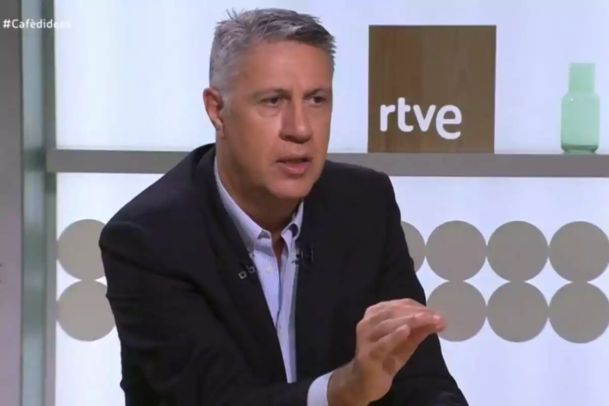 Hombre de cabello canoso y corto hablando en un programa de televisión con el logo de rtve al fondo