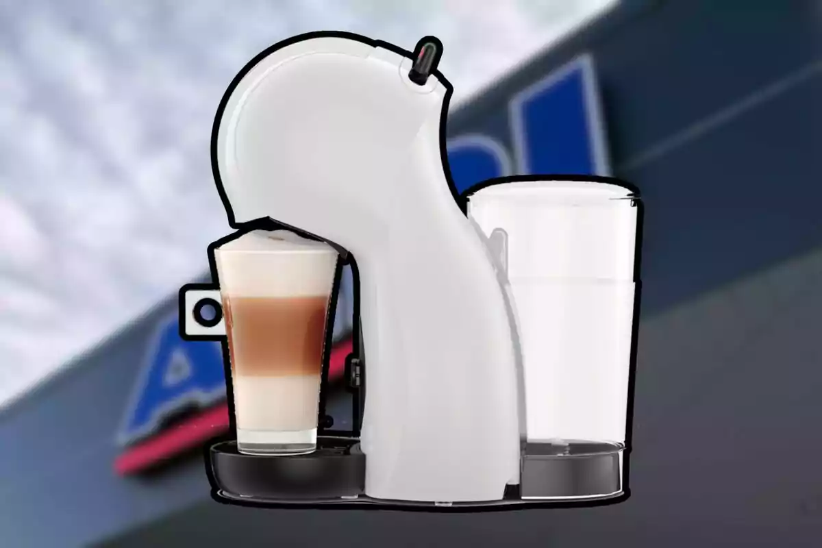 Cafetera blanca de cápsulas con un vaso de café con leche espumosa frente a un fondo borroso de una tienda.