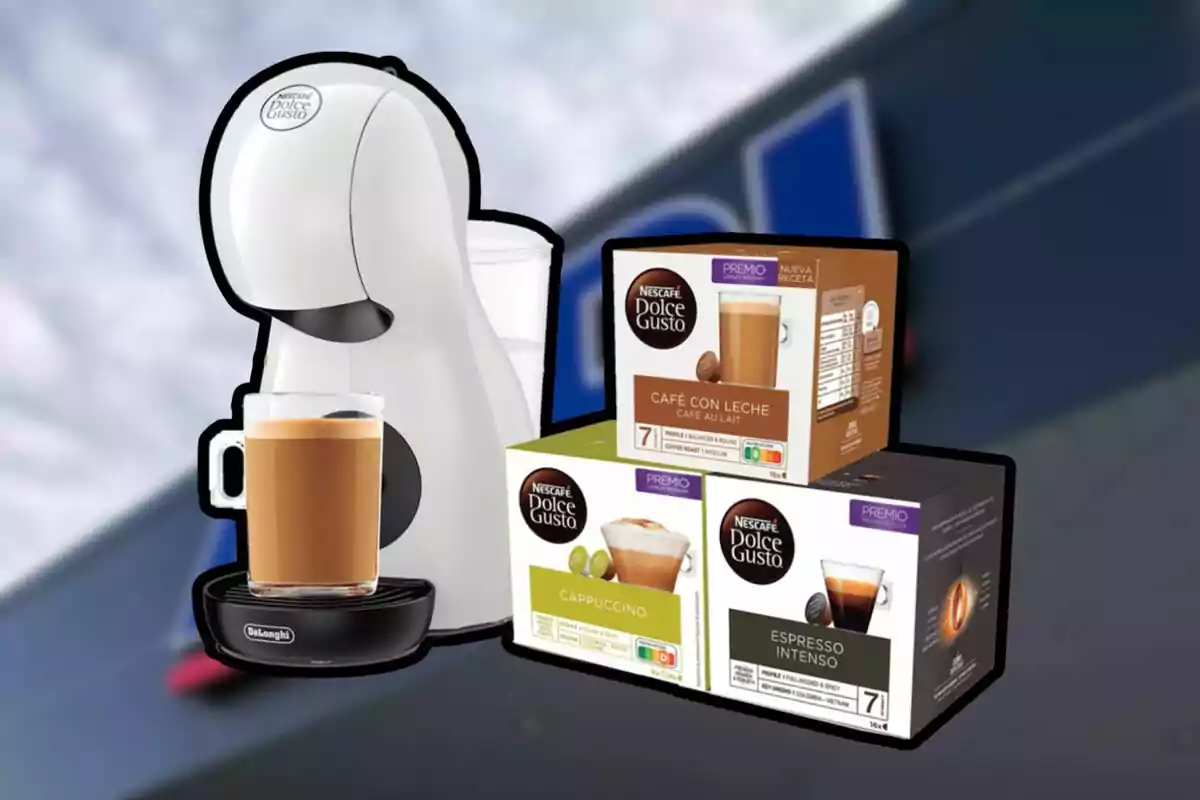 Cafetera blanca Nescafé Dolce Gusto con una taza de café y tres cajas de cápsulas de diferentes sabores frente a un fondo desenfocado.