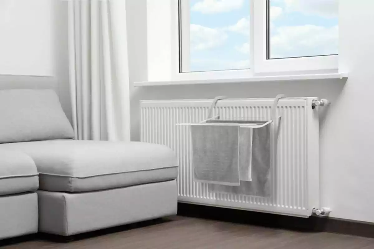 Tovalloles grises penjades en un estenedor sobre un radiador blanc al costat d’un sofà en una sala moderna i lluminosa