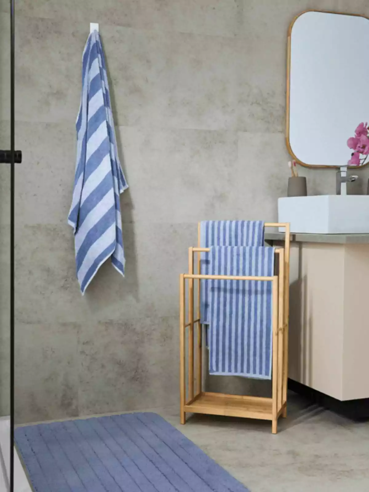 Baño moderno con toallas azules a rayas, tapete azul y mueble de madera junto a un lavabo blanco con espejo rectangular