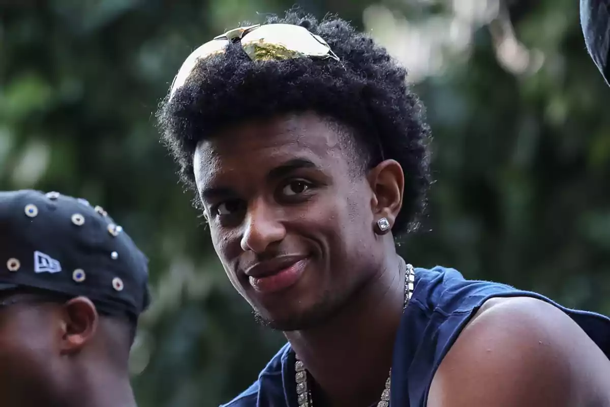 Alejandro Balde amb ulleres de sol al cap, samarreta de tirants blava i collaret platejat, somrient a l’aire lliure