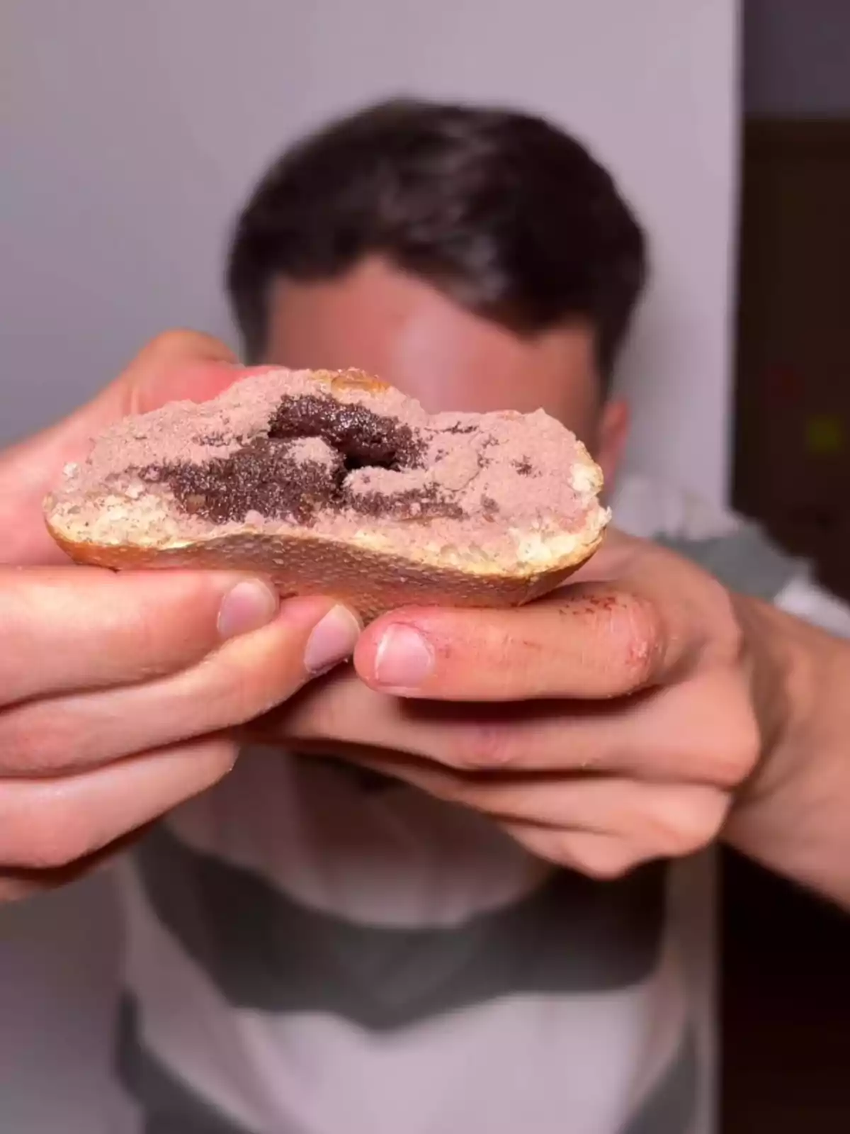 Alejandro Jara sostenint un pa partit per la meitat amb farciment i cobertura de xocolata en primer pla