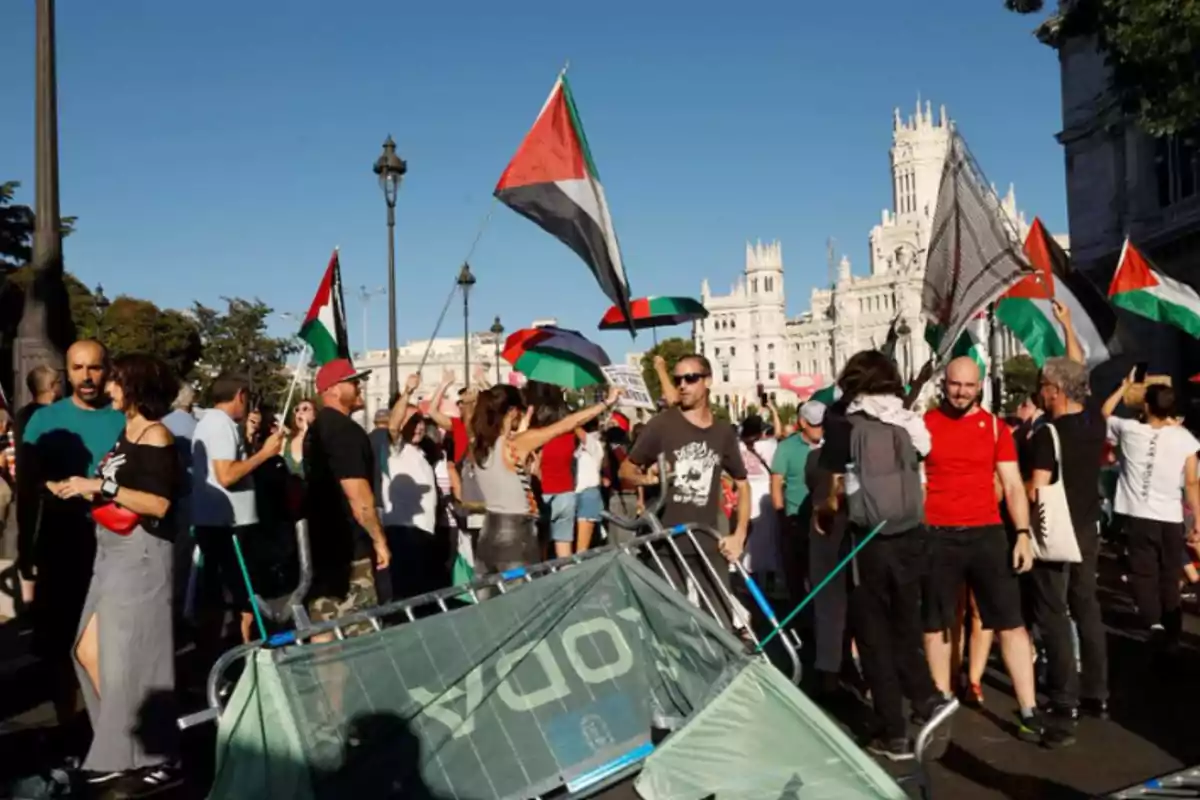 Manifestació en una plaça amb persones onejant banderes palestines i una tanca caiguda en primer pla