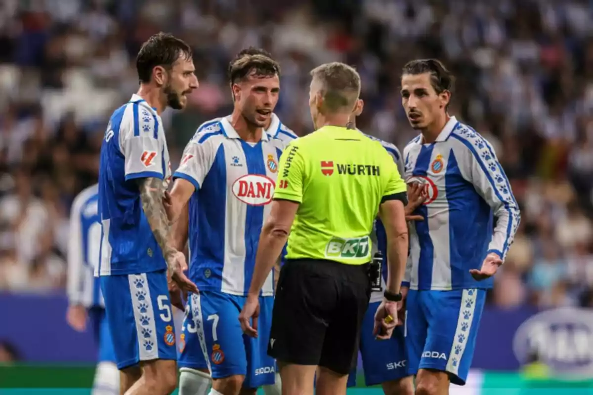 Tres jugadors de l’RCDE Espanyol amb uniforme blau i blanc discuteixen amb l’àrbitre Alejandro Hernández Hernández vestit de groc al mig d’un partit Tres jugadors de l’RCDE Espanyol amb uniforme blau i blanc discuteixen amb l’àrbitre Alejandro Hernández Hernández vestit de groc al mig d’un partit