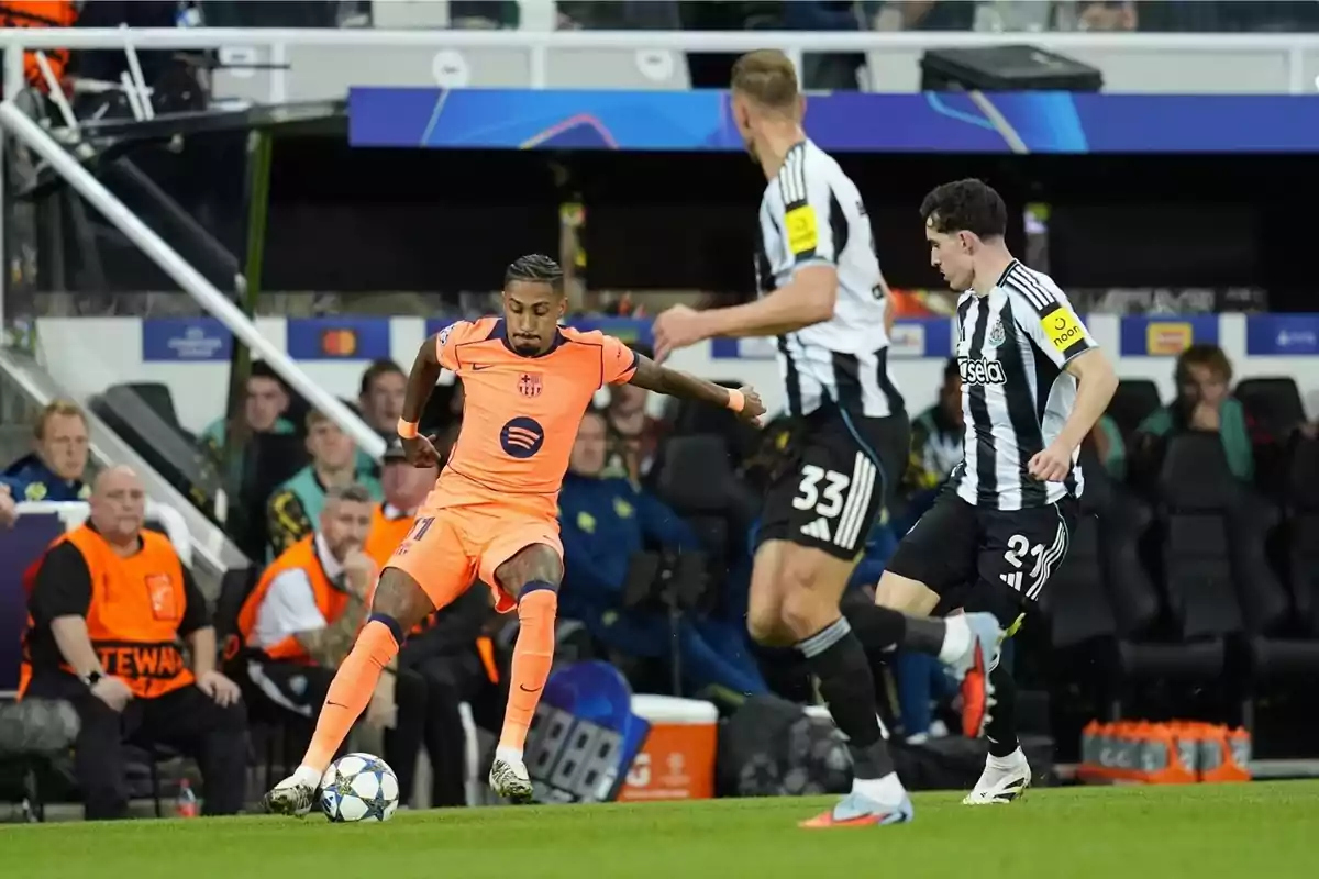 Un jugador del Barcelona amb uniforme taronja controla la pilota mentre dos jugadors del Newcastle intenten defensar durant un partit de futbol. Un jugador del Barcelona amb uniforme taronja controla la pilota mentre dos jugadors del Newcastle intenten defensar durant un partit de futbol.