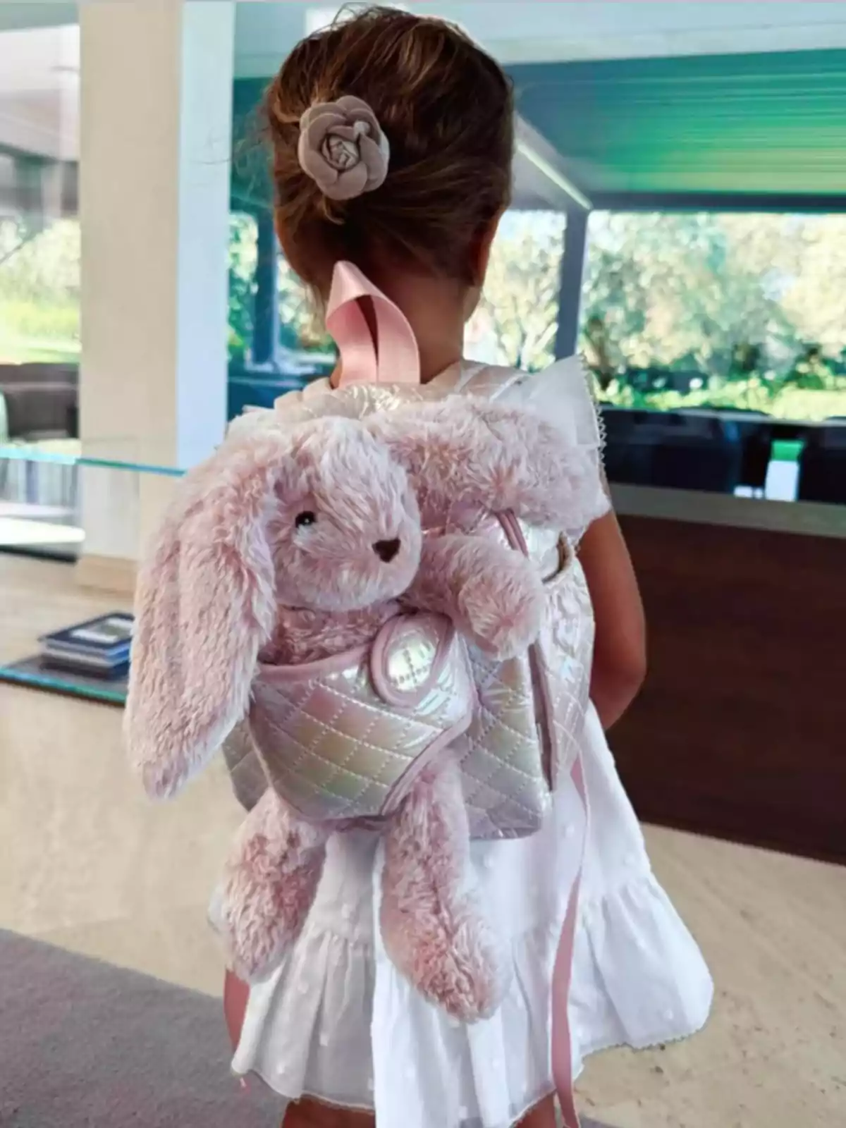 Bella Morata Campello d’esquena amb vestit blanc i monyo als cabells porta una motxilla de peluix en forma de conill rosa Bella Morata Campello d’esquena amb vestit blanc i monyo als cabells porta una motxilla de peluix en forma de conill rosa