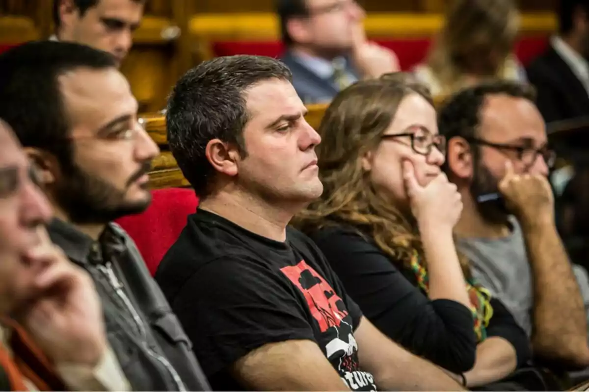 Persones assegudes en una sala amb expressió seriosa i atenta