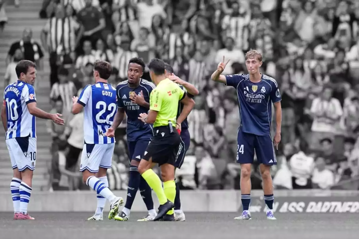 Jugadors de futbol de dos equips discuteixen amb l’àrbitre al camp mentre un jugador amb uniforme blau fosc fa un senyal de pau amb la mà i el fons és en blanc i negre. Jugadors de futbol de dos equips discuteixen amb l’àrbitre al camp mentre un jugador amb uniforme blau fosc fa un senyal de pau amb la mà i el fons és en blanc i negre.
