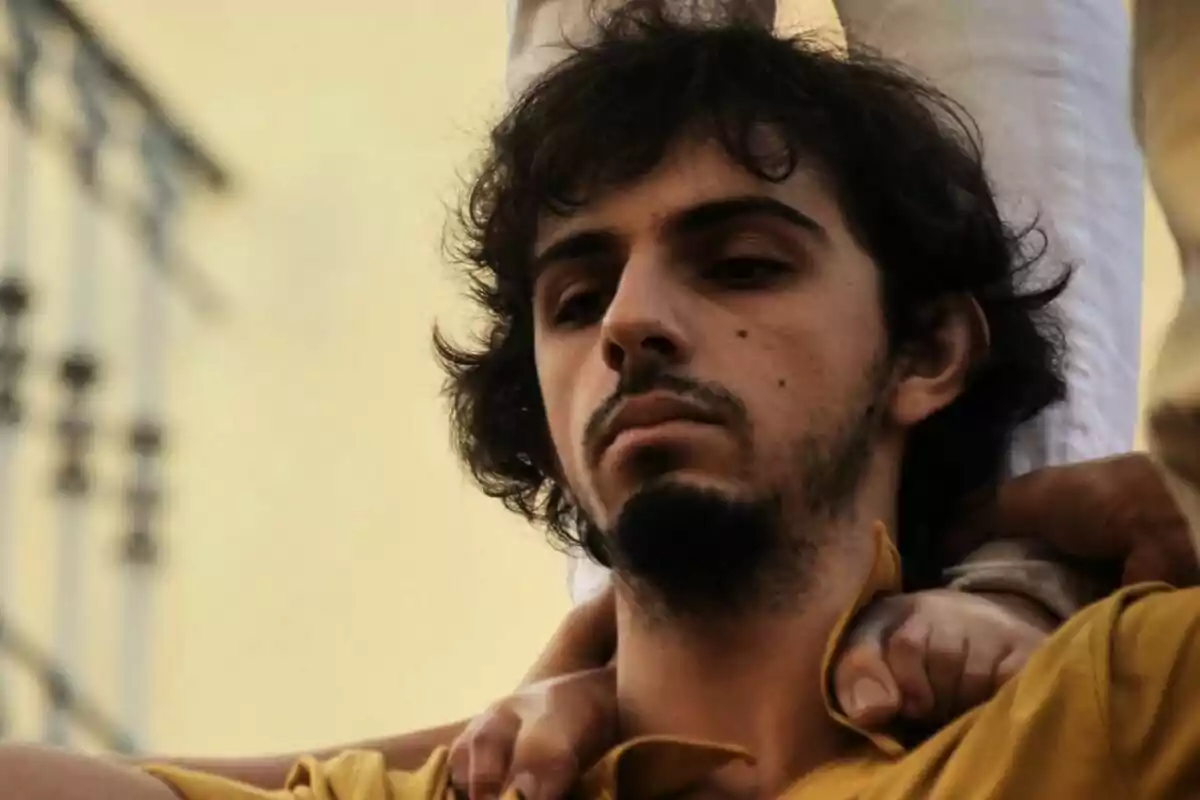 Joven con expresión seria sostiene a otra persona sobre sus hombros durante una actividad grupal Joven con expresión seria sostiene a otra persona sobre sus hombros durante una actividad grupal