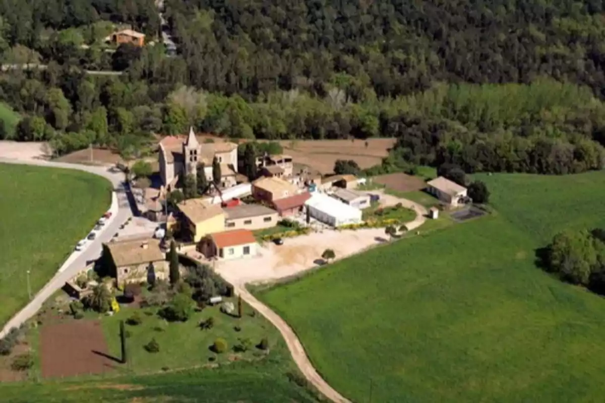 Vista aèria d’un petit poble, Estanyol, envoltat de camps verds i arbres, amb diverses cases i una església al centre Vista aèria d’un petit poble, Estanyol, envoltat de camps verds i arbres, amb diverses cases i una església al centre
