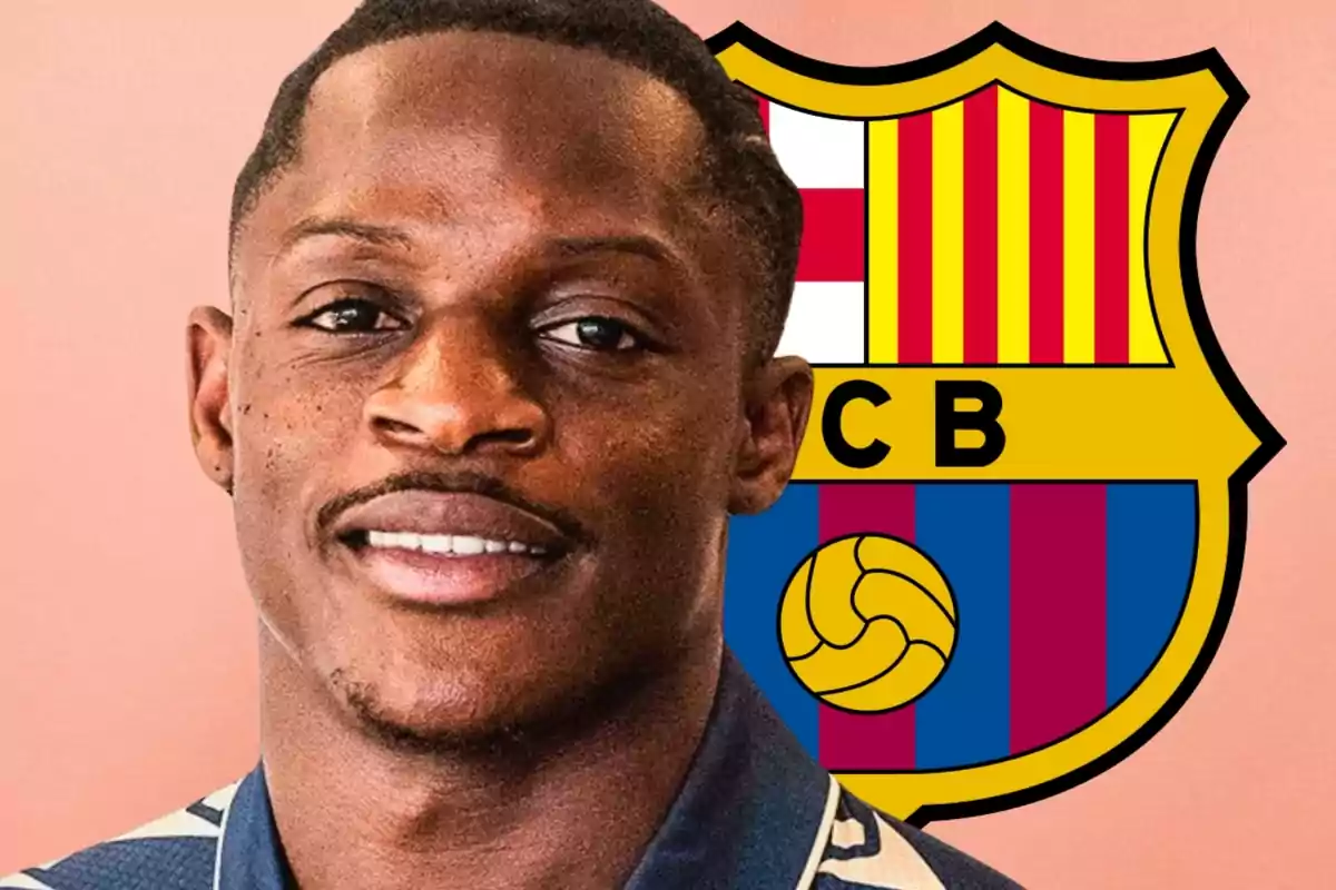 Un home somrient amb una camisa blava posant davant de l’escut del FC Barcelona sobre un fons rosat