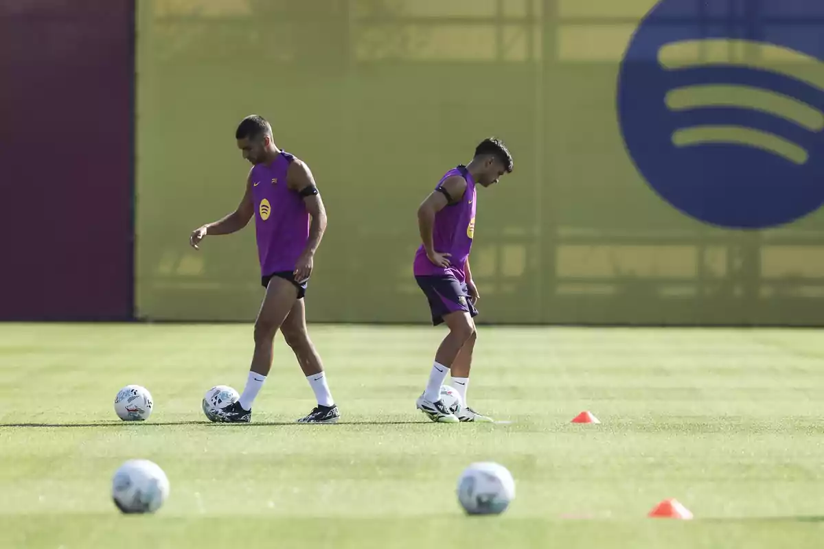 Ferran Torres i Pedri entrenen en un camp de gespa amb pilotes i cons taronges, tots dos porten uniforme d’entrenament morat i de fons hi ha el logotip de Spotify. Ferran Torres i Pedri entrenen en un camp de gespa amb pilotes i cons taronges, tots dos porten uniforme d’entrenament morat i de fons hi ha el logotip de Spotify.