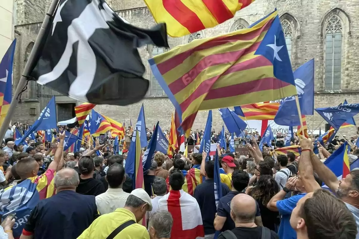 Manifestación con una multitud de personas ondeando banderas catalanas y esteladas frente a un edificio antiguo Manifestación con una multitud de personas ondeando banderas catalanas y esteladas frente a un edificio antiguo