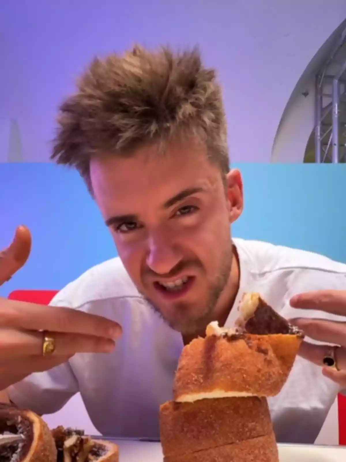 Valgardi con expresión divertida señalando un pastel apilado frente a él en una mesa Valgardi con expresión divertida señalando un pastel apilado frente a él en una mesa