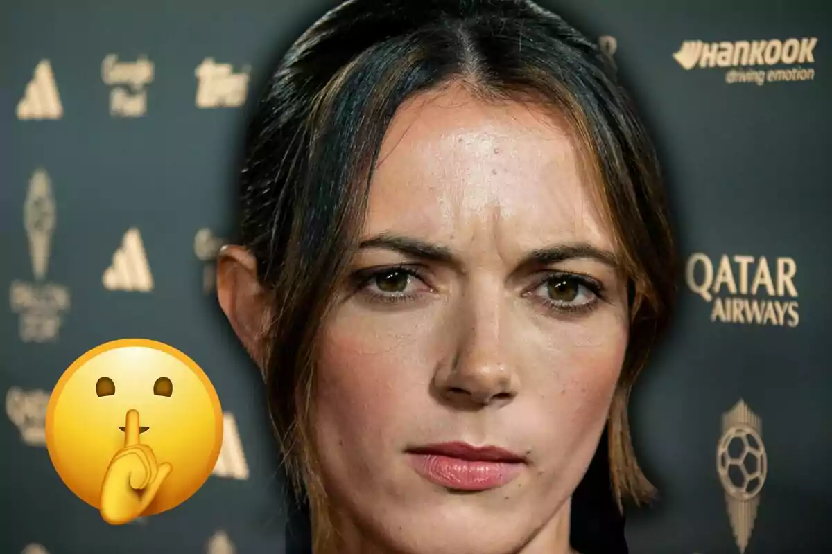 Dona d’expressió seriosa en un esdeveniment amb un fons de logotips i un emoji de silenci a la cantonada esquerra